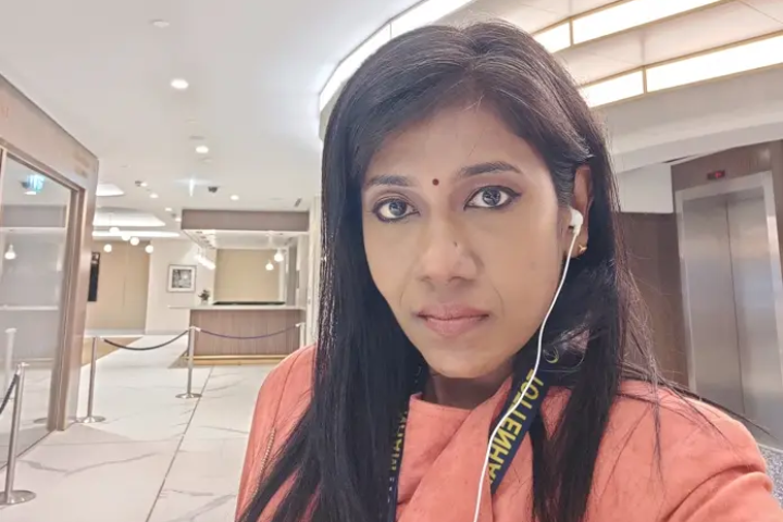 a selfie of Kogilavani wearing earbuds and an orange top in an office building