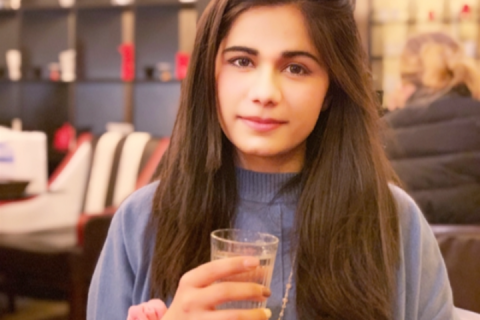 Fatima in a blue jumper holding a coffee cup